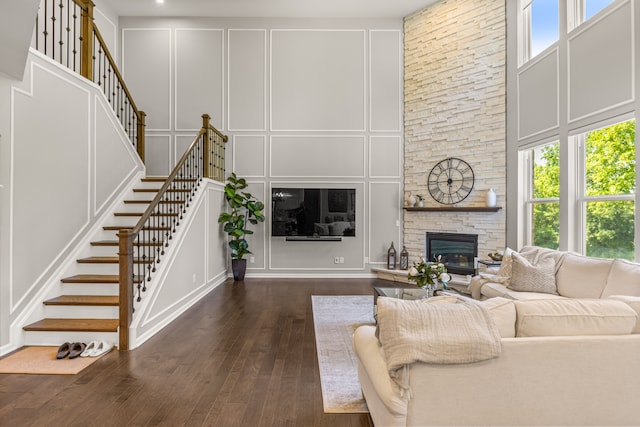 living room with a stone fireplace, plenty of natural light, a high ceiling, and dark hardwood / wood-style floors