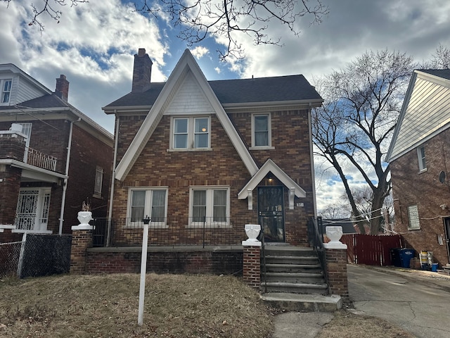 tudor home with brick siding, a chimney, and fence