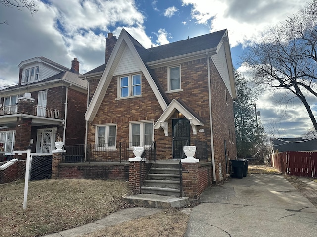 english style home featuring a porch, brick siding, fence, and a chimney