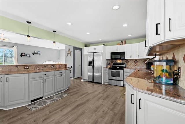 kitchen featuring stone counters, hanging light fixtures, wood-type flooring, white cabinets, and appliances with stainless steel finishes