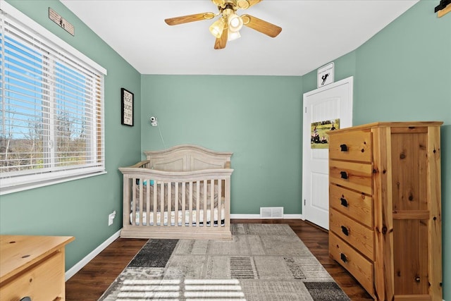 bedroom with a crib, dark hardwood / wood-style floors, and ceiling fan