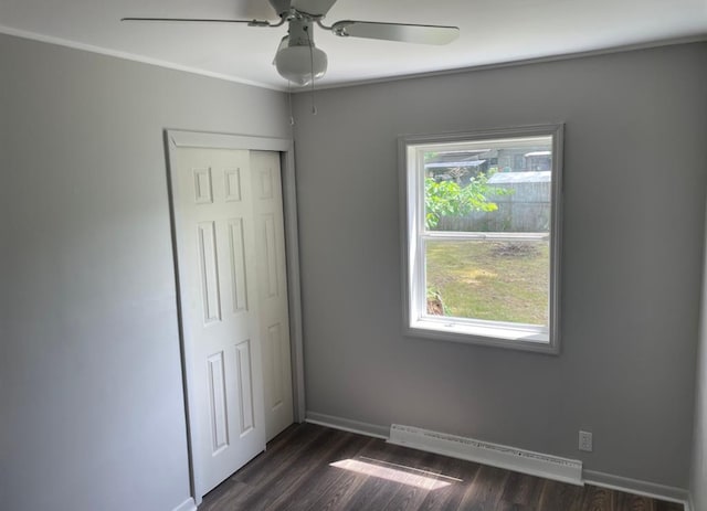 unfurnished bedroom with ceiling fan, a closet, dark hardwood / wood-style floors, and a baseboard heating unit