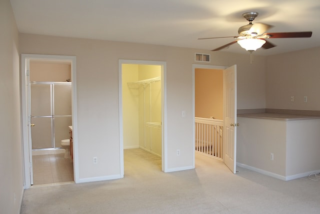 unfurnished bedroom featuring ceiling fan, ensuite bathroom, a walk in closet, light carpet, and a closet