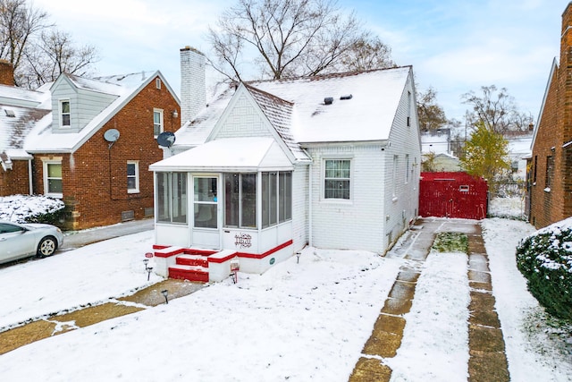 snow covered rear of property with a sunroom