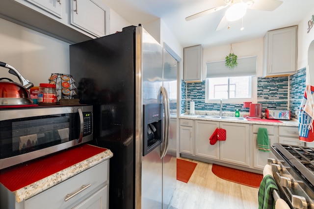 kitchen with light stone countertops, sink, stainless steel appliances, light hardwood / wood-style flooring, and decorative backsplash