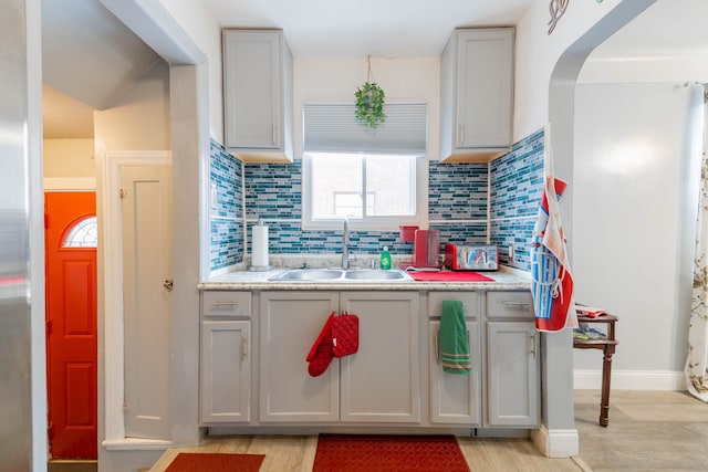 kitchen with backsplash, gray cabinets, light hardwood / wood-style flooring, and sink