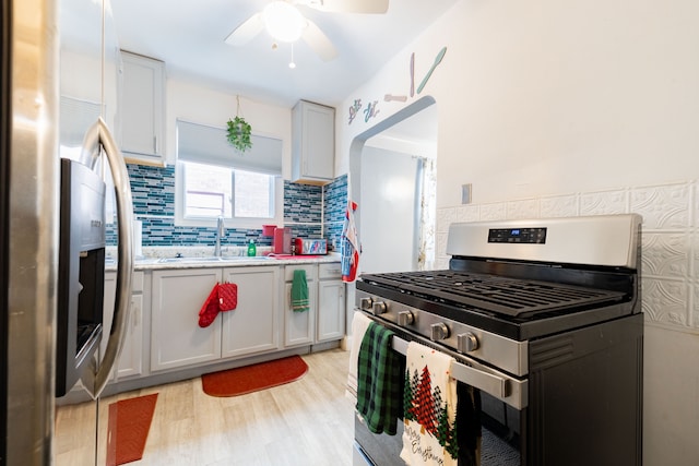 kitchen with white cabinets, sink, decorative backsplash, light wood-type flooring, and appliances with stainless steel finishes