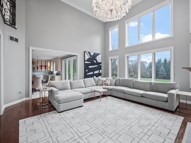 living room with a healthy amount of sunlight, a towering ceiling, wood-type flooring, and an inviting chandelier