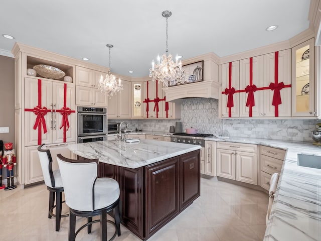 kitchen with light stone counters, backsplash, an island with sink, a chandelier, and a breakfast bar area