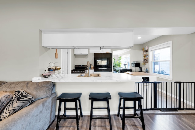 kitchen featuring white cabinetry, sink, dark wood-type flooring, a kitchen breakfast bar, and kitchen peninsula