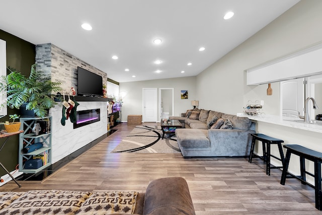 living room with a large fireplace, light hardwood / wood-style floors, vaulted ceiling, and sink