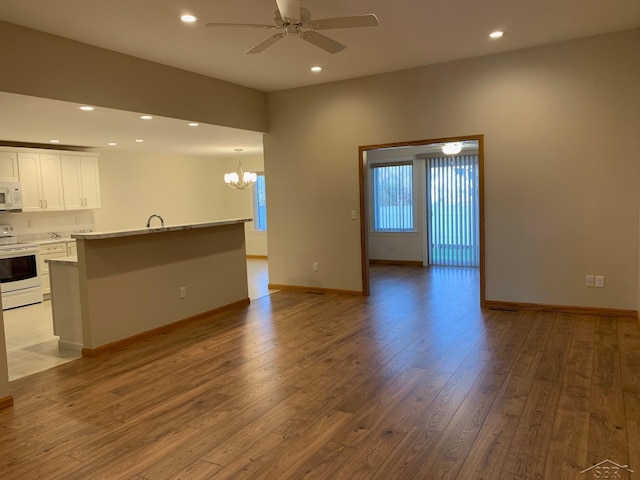 unfurnished living room featuring ceiling fan with notable chandelier, light wood-type flooring, and sink