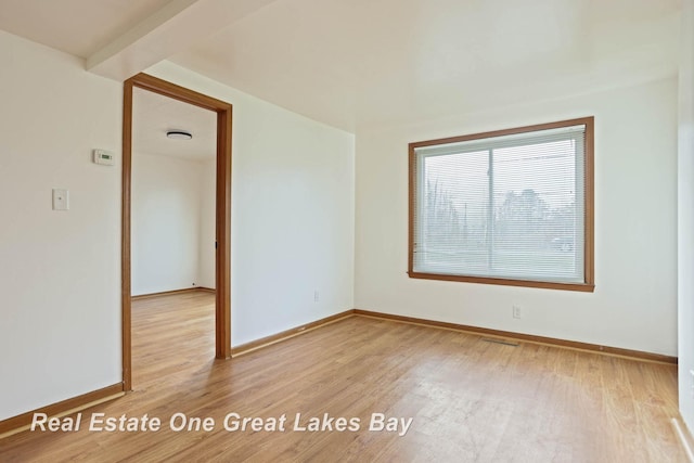 empty room featuring beam ceiling and light hardwood / wood-style flooring