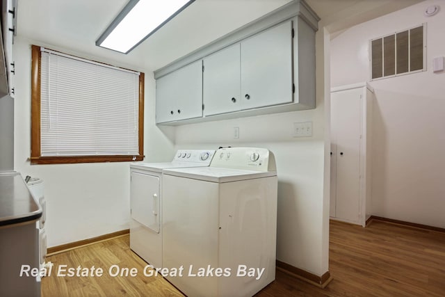 clothes washing area with light hardwood / wood-style floors, washing machine and dryer, and cabinets