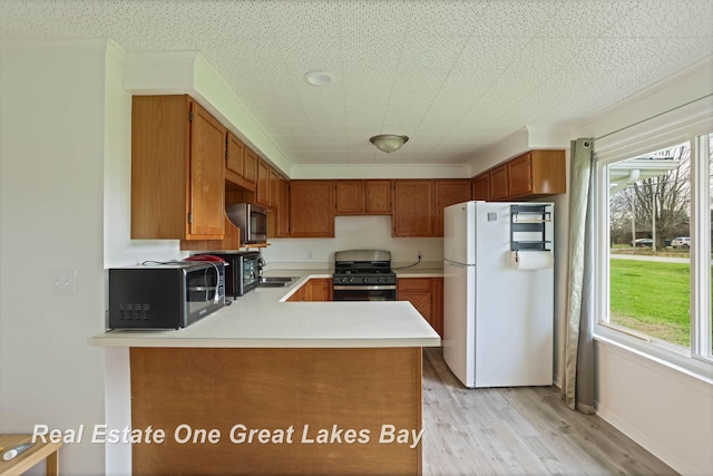 kitchen with white fridge, light hardwood / wood-style floors, sink, kitchen peninsula, and gas range oven