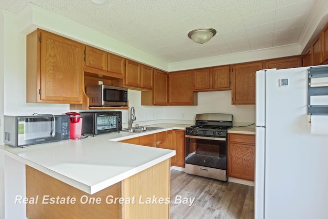 kitchen with white refrigerator, sink, kitchen peninsula, gas range, and light hardwood / wood-style flooring