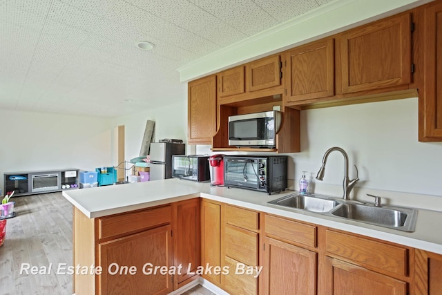 kitchen featuring appliances with stainless steel finishes, sink, light hardwood / wood-style floors, and kitchen peninsula