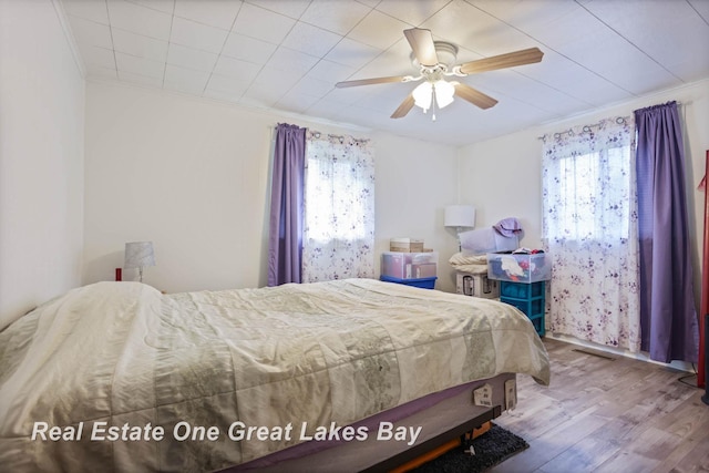 bedroom with ceiling fan, wood-type flooring, multiple windows, and ornamental molding