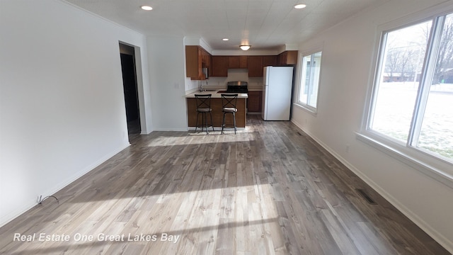 kitchen with sink, white fridge, ornamental molding, a kitchen bar, and light wood-type flooring