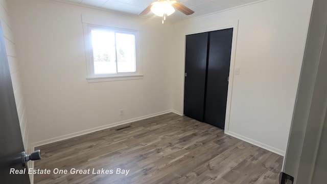 unfurnished bedroom featuring ceiling fan, a closet, crown molding, and hardwood / wood-style flooring