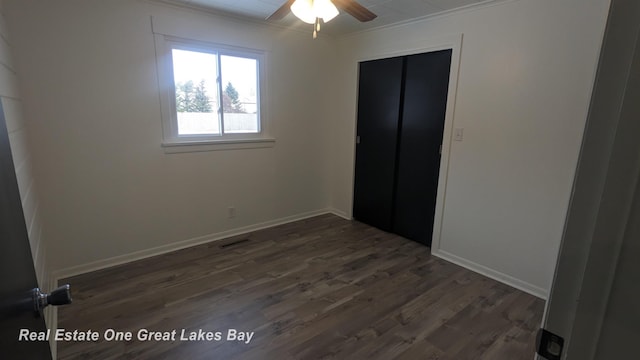 unfurnished bedroom with ceiling fan, a closet, dark wood-type flooring, and crown molding