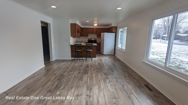 kitchen featuring a center island, a breakfast bar, light wood-type flooring, stainless steel range, and white refrigerator