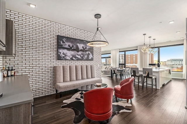 living room featuring sink, dark hardwood / wood-style flooring, an inviting chandelier, and brick wall