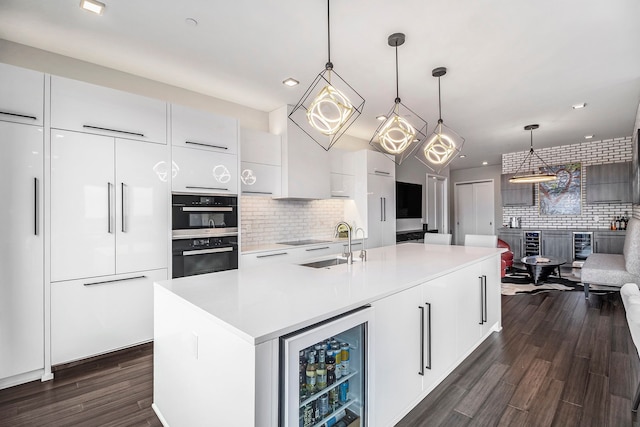 kitchen with wine cooler, a kitchen island with sink, dark wood-type flooring, pendant lighting, and white cabinetry