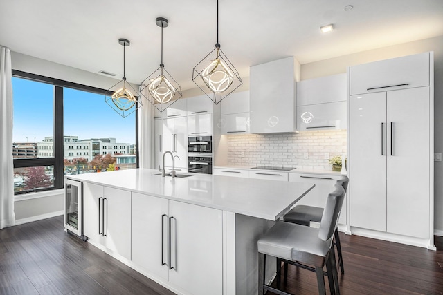 kitchen featuring sink, dark hardwood / wood-style floors, pendant lighting, a kitchen island with sink, and white cabinets