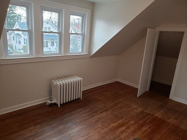 bonus room featuring lofted ceiling, radiator, and dark hardwood / wood-style flooring