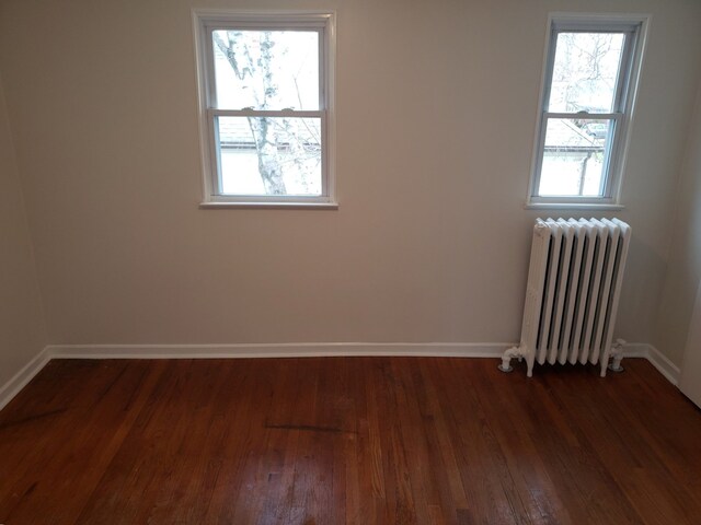 empty room featuring dark wood-type flooring and radiator heating unit