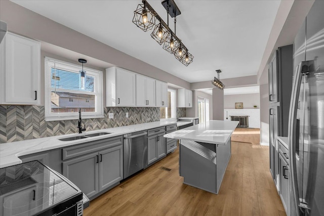 kitchen with gray cabinetry, decorative light fixtures, light wood-type flooring, and stainless steel appliances