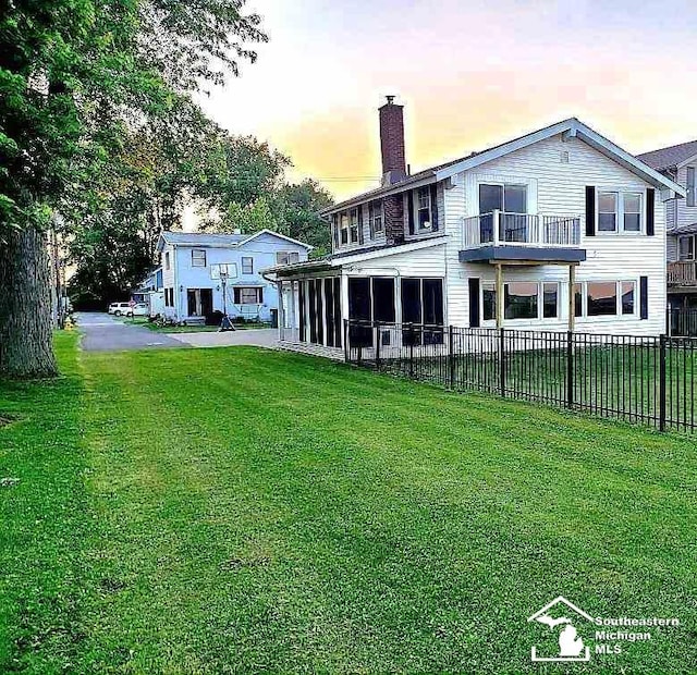 back house at dusk featuring a lawn, a sunroom, and a balcony