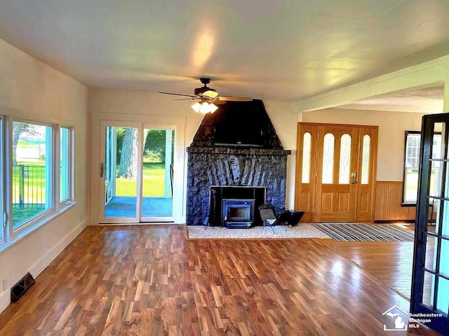 unfurnished living room with a fireplace, a ceiling fan, visible vents, wainscoting, and wood finished floors
