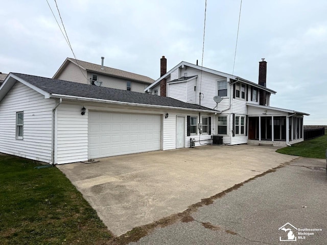 back of property featuring a sunroom, driveway, an attached garage, and a chimney