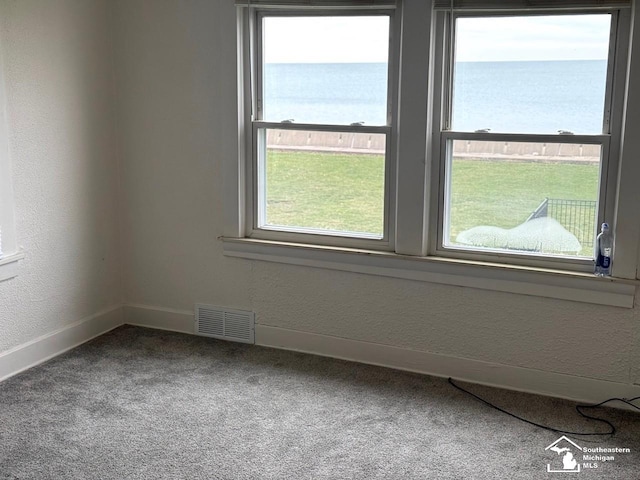 spare room featuring carpet flooring, a water view, visible vents, a textured wall, and baseboards