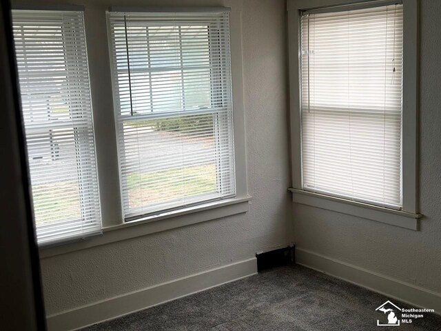 spare room featuring dark carpet, a healthy amount of sunlight, and baseboards