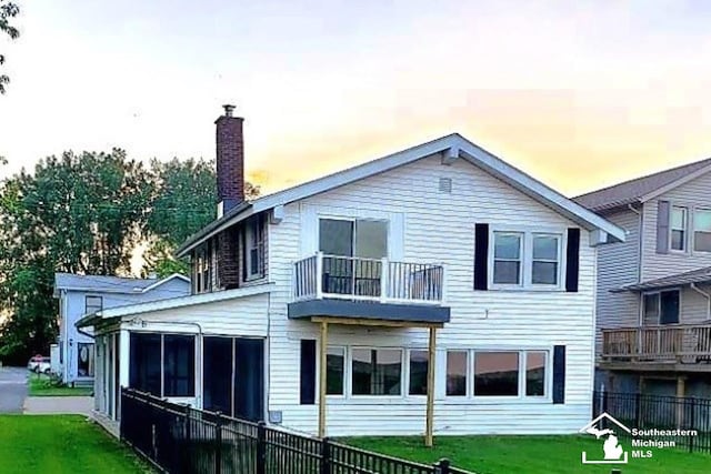 rear view of property featuring a chimney, fence, a balcony, and a lawn
