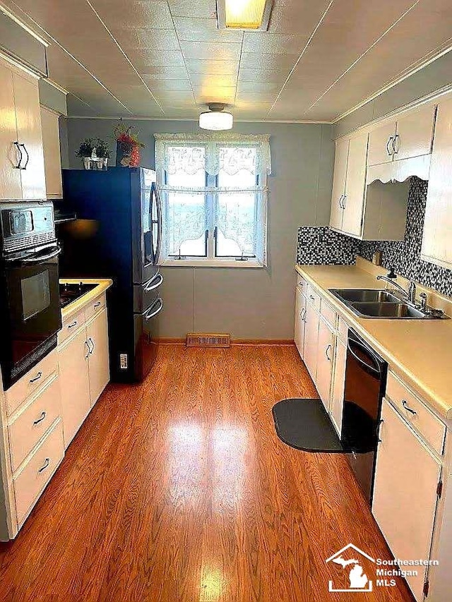 kitchen featuring sink, light hardwood / wood-style floors, white cabinetry, and black appliances