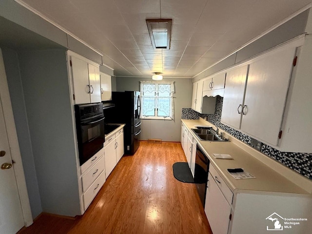 kitchen featuring a sink, tasteful backsplash, light wood-type flooring, black appliances, and white cabinets