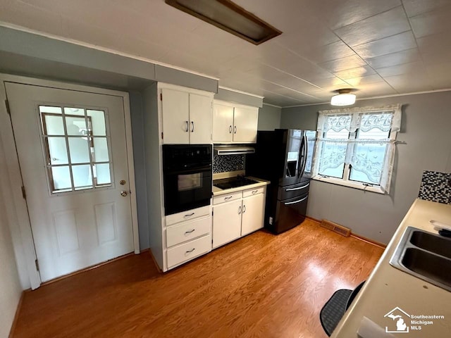 kitchen featuring white cabinets, a sink, visible vents, black appliances, and light wood finished floors