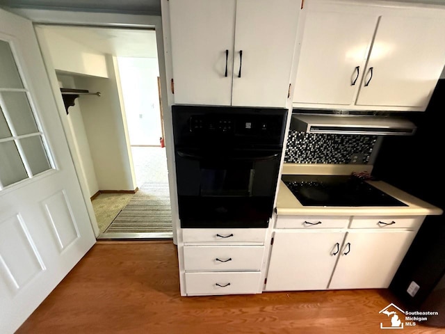 interior space featuring black appliances, exhaust hood, white cabinets, and wood finished floors