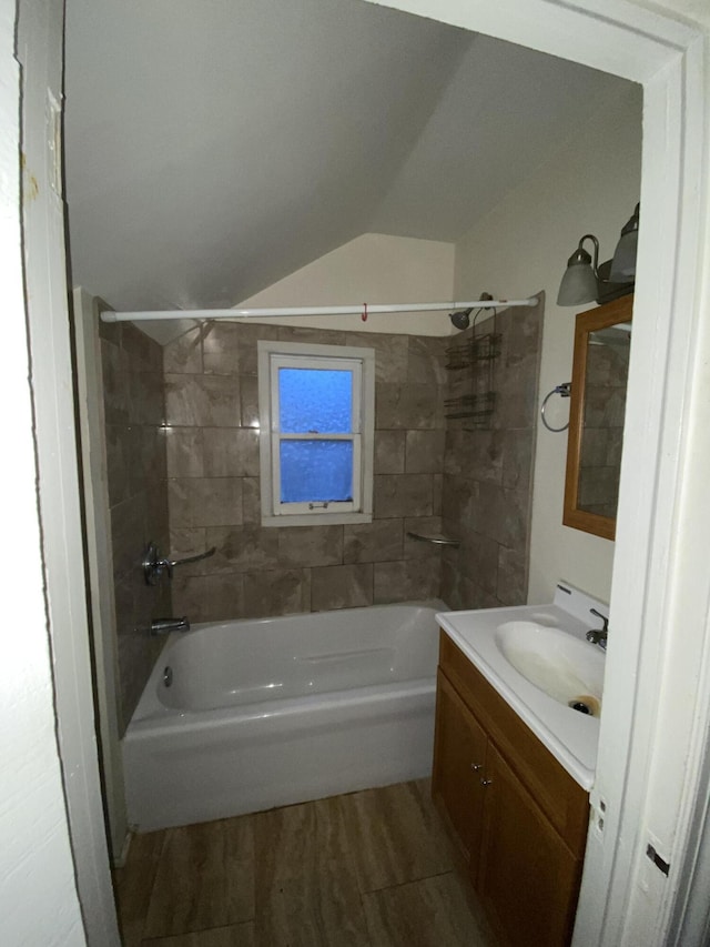 bathroom with hardwood / wood-style flooring, vanity, lofted ceiling, and tiled shower / bath