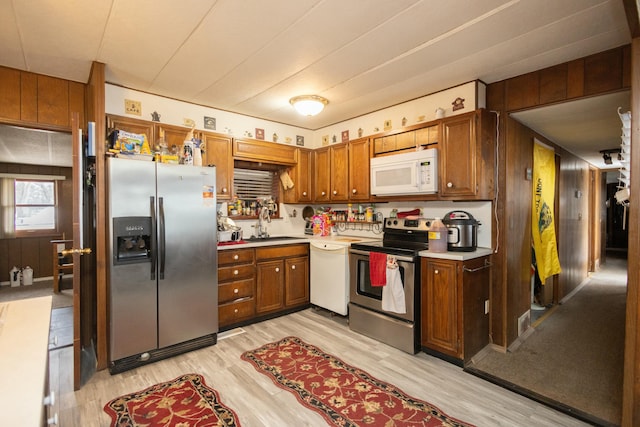 kitchen featuring appliances with stainless steel finishes, light hardwood / wood-style flooring, wooden walls, and sink