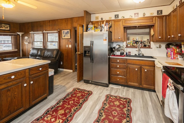 kitchen with ceiling fan, sink, stainless steel appliances, wooden walls, and light wood-type flooring