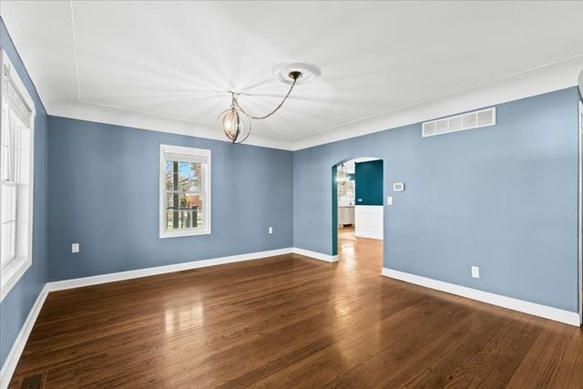 empty room featuring dark wood-type flooring, a healthy amount of sunlight, and a notable chandelier