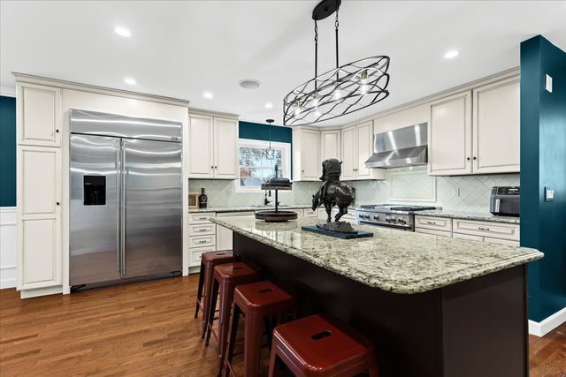 kitchen featuring stove, stainless steel built in fridge, hanging light fixtures, wall chimney exhaust hood, and a kitchen island