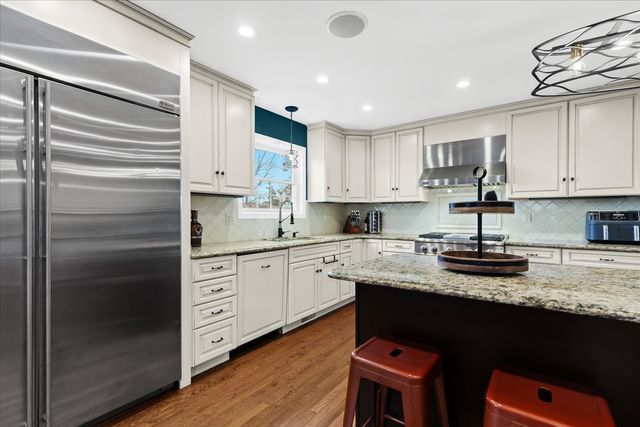 kitchen with sink, wall chimney range hood, dark hardwood / wood-style floors, built in refrigerator, and decorative light fixtures