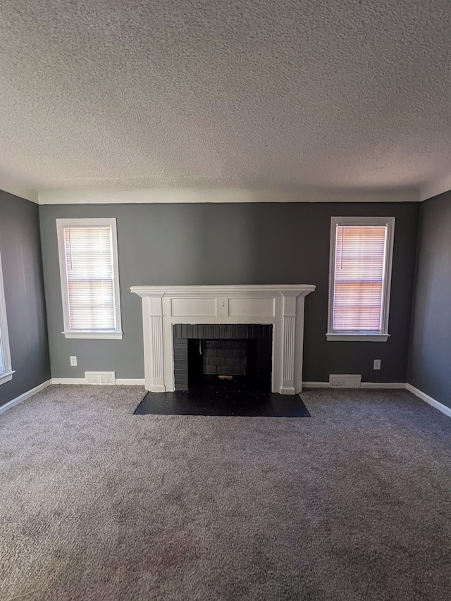 unfurnished living room with dark carpet, a textured ceiling, and a brick fireplace