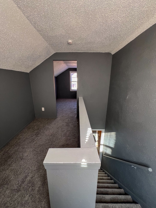 staircase featuring lofted ceiling, carpet floors, and a textured ceiling